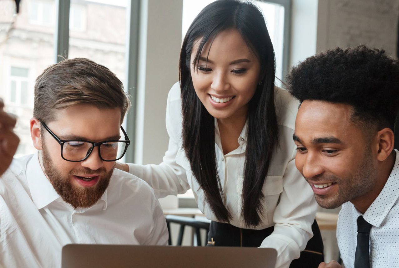 A group of colleagues gathered around a laptop, smiling while reviewing information together.